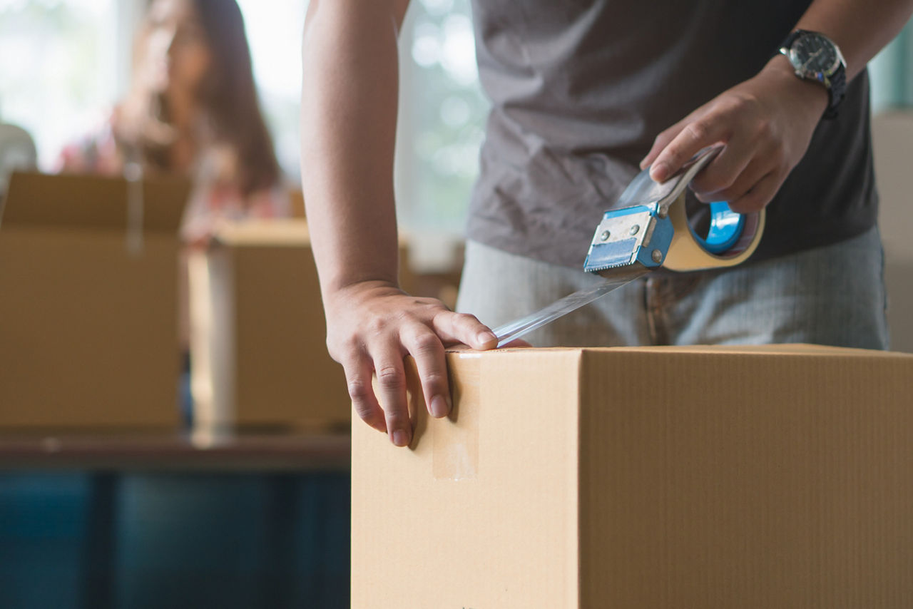 Man sealing a moving box with clear tape | Blog | Greystar 